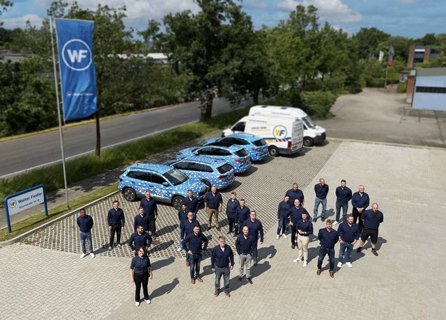 Die Mitarbeitenden von Walter Fiedler stehen auf dem Parkplatz in Form der Zahl 100