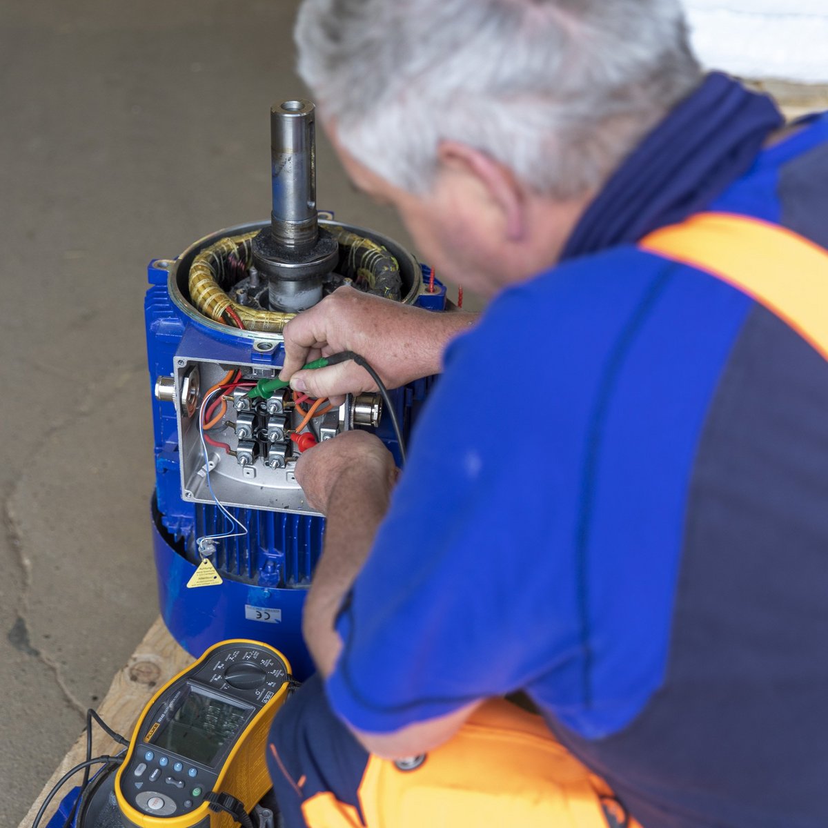 Ein Techniker arbeitet konzentriert an einem elektrischen Motor, während er Kabel und Verbindungen überprüft.