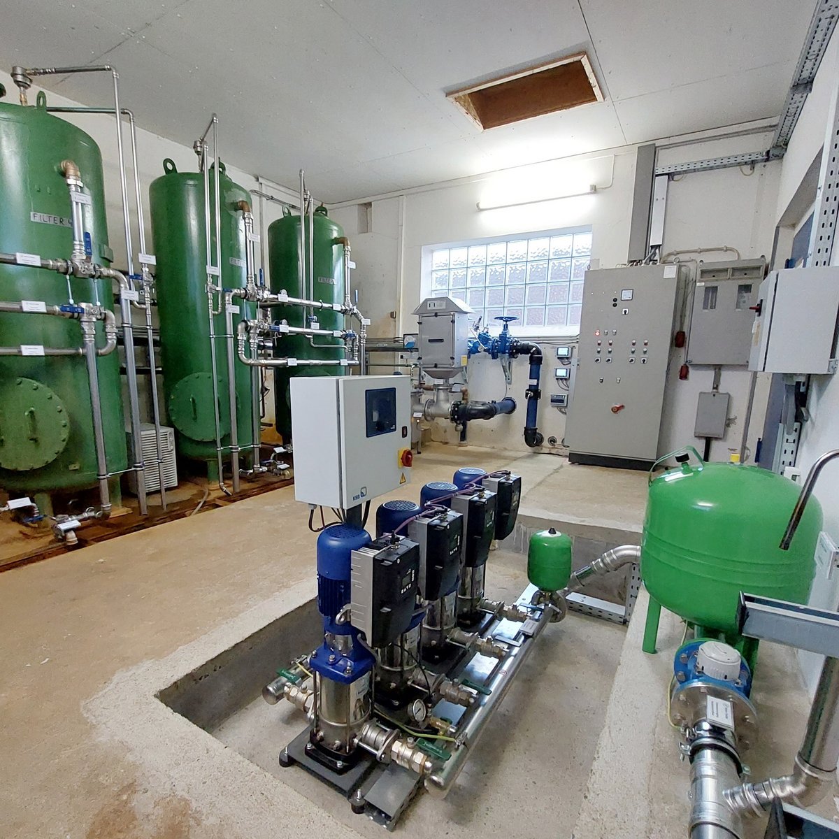 Im Hintergrund sind grüne Filtertanks zu sehen, während im Vordergrund eine Reihe von Pumpen für die Wasserzirkulation bereitsteht.