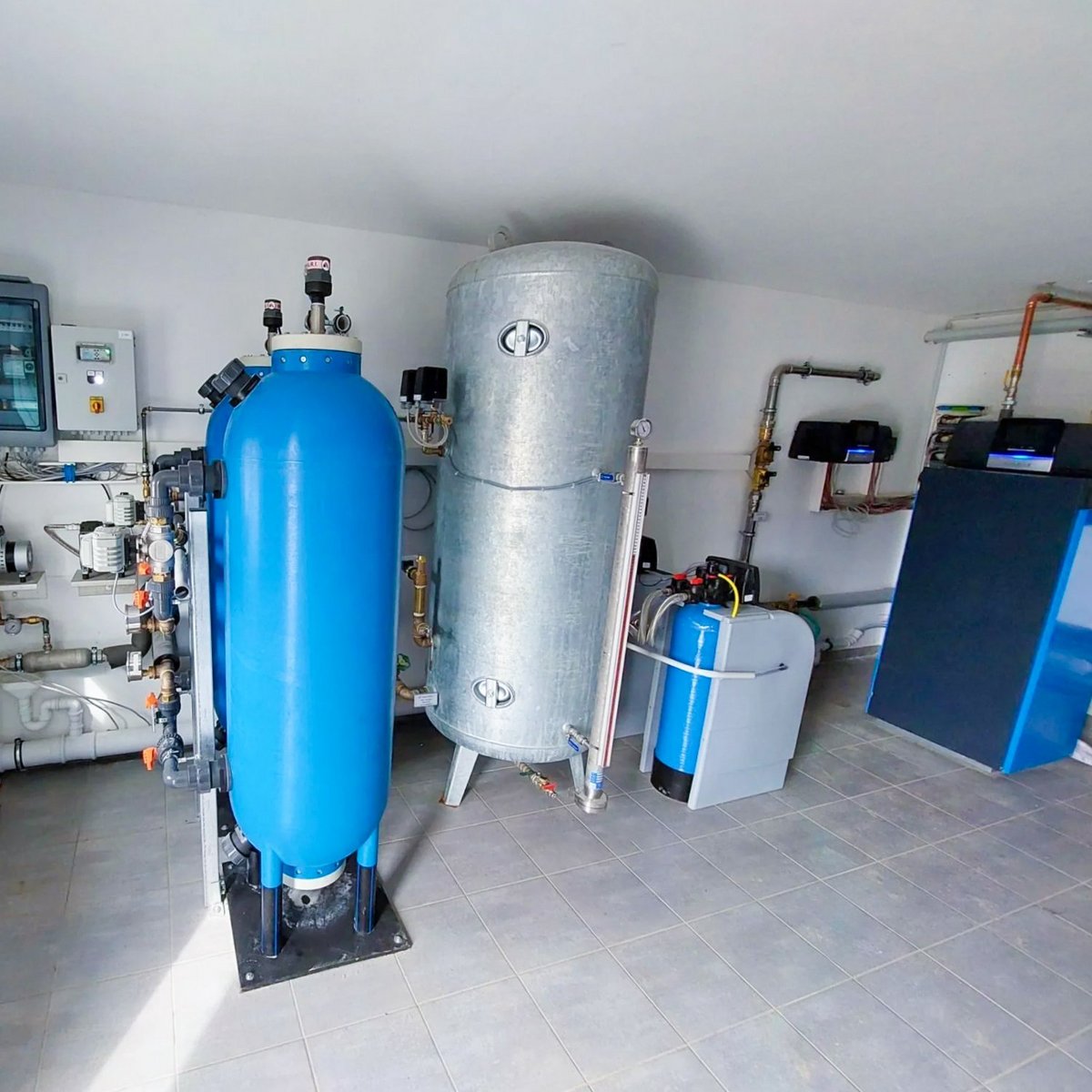Ein Raum mit verschiedenen Wasseraufbereitungsanlagen, darunter ein großer blauer Tank und ein silberner Wassertank.